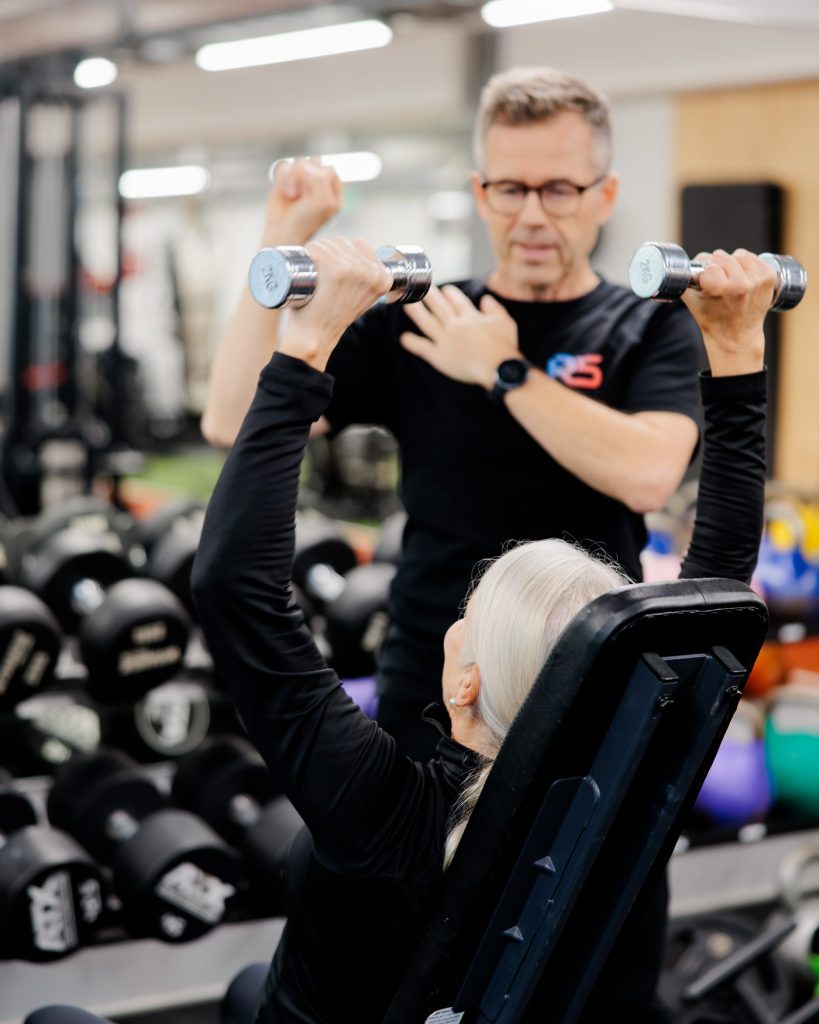 Jerry Ketola spotting a client during a dumbbell shoulder press at the gym